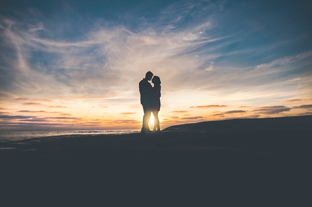 Muž a žena v objatí sa bozkávajú na kopci pri západe slnka